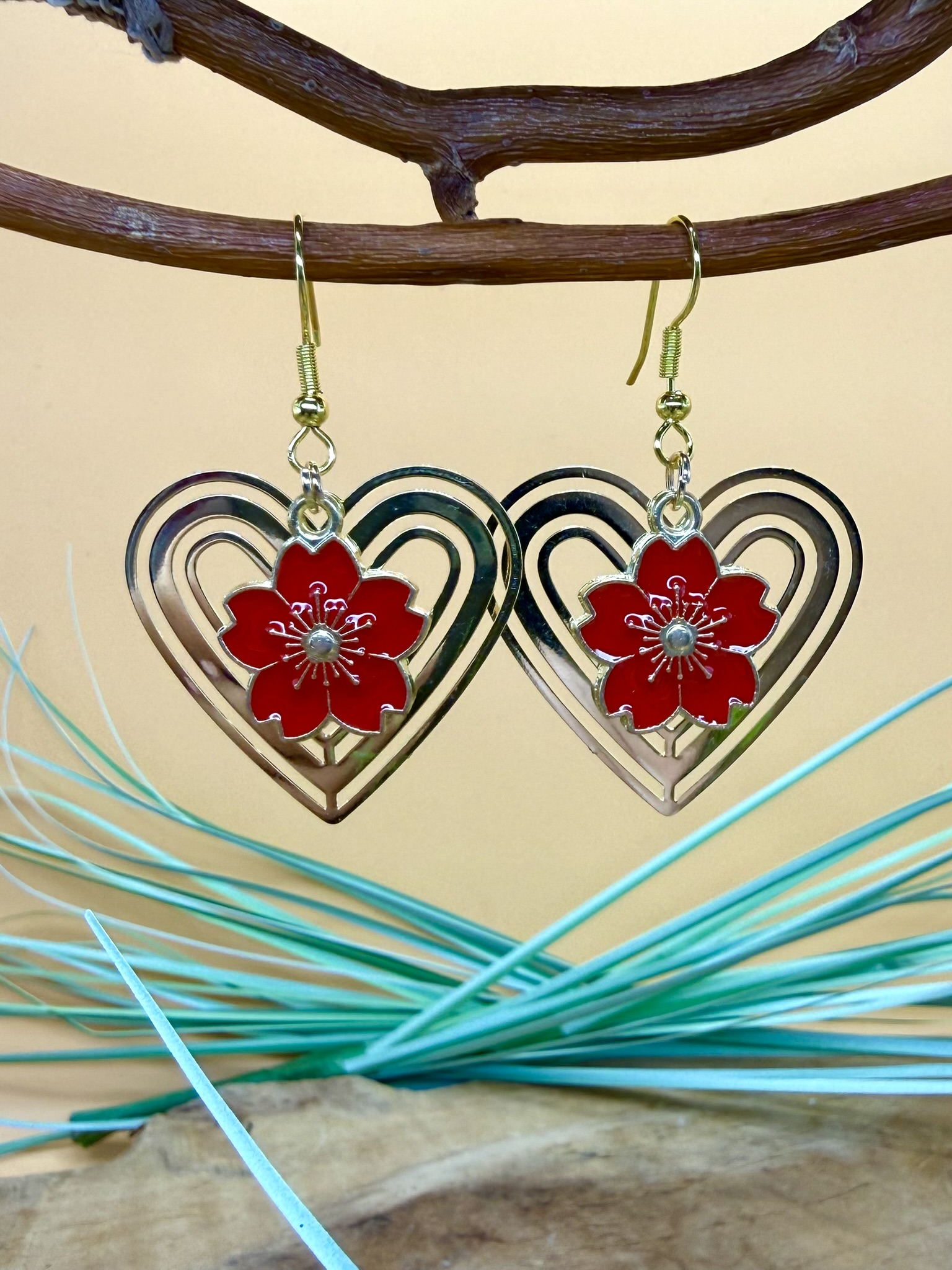 Boucles d'oreilles fleur rouge Sakura avec fleur rouge en métal émaillé suspendue dans une estampe cœur dorée ajourée et crochets en acier inoxydable