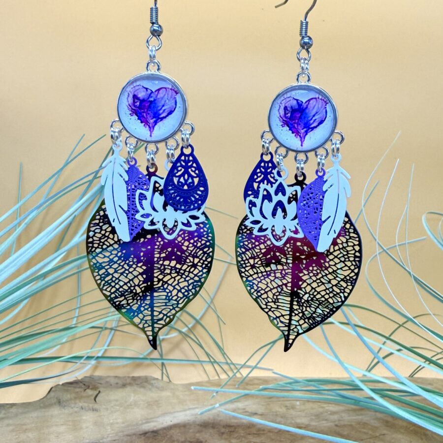 Boucles d'oreilles Aélia avec cabochon cœur violet, feuille iridescente aux reflets changeants, plume blanche, fleur de lotus blanche et crochets en acier inoxydable.