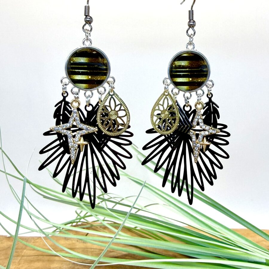 Boucles d'oreilles noir et doré avec cabochon rond, estampe noire ajourée, breloque goutte dorée à motif floral et étoile en strass contour doré.
