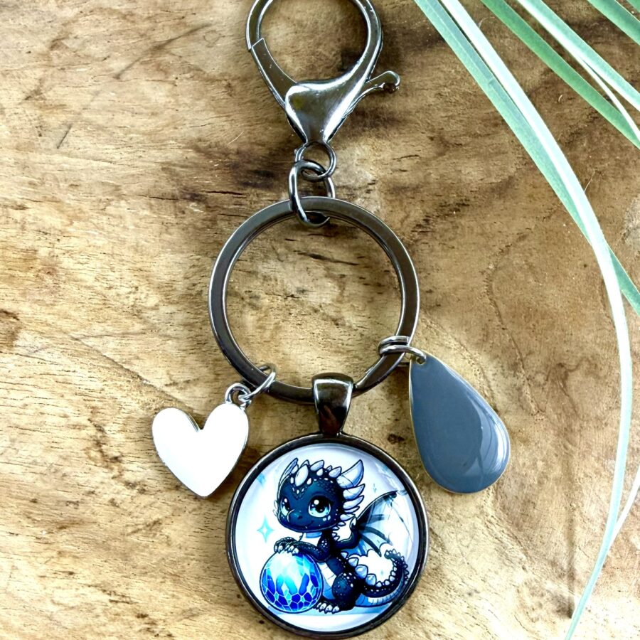 Porte-clés dragon en acier inoxydable avec cabochon de 25 mm représentant un bébé dragon bleu avec son œuf, breloque cœur blanc et breloque goutte grise.