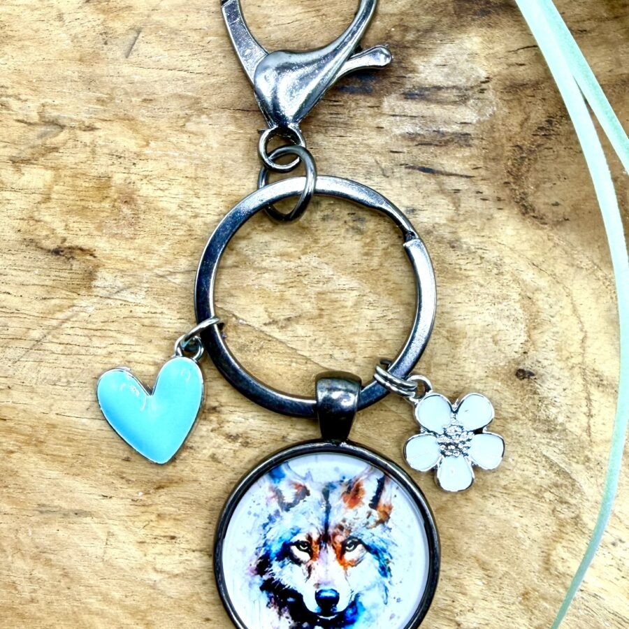 Porte-clés loup en acier inoxydable avec cabochon de 25 mm représentant un loup aux nuances bleutées, breloque cœur turquoise et fleur blanche émaillée.